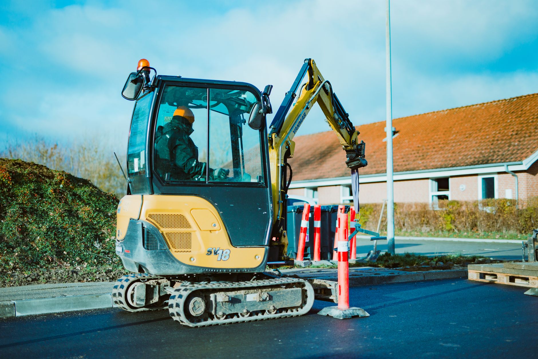Minigraver aan het werk langs een stoep in een woonwijk
