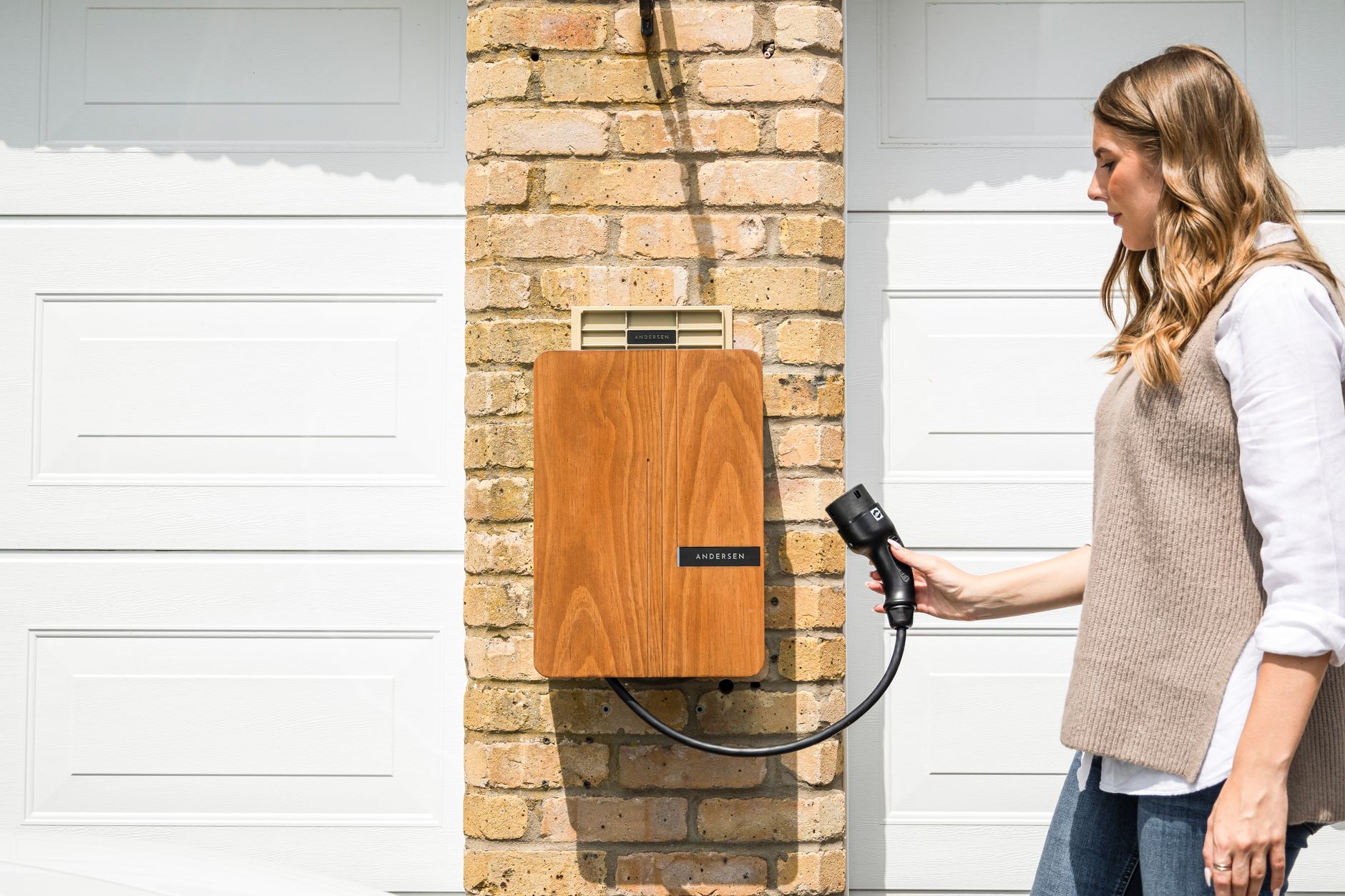Vrouw pakt de laadkabel van een laadpaal aan de gevel naast de garage